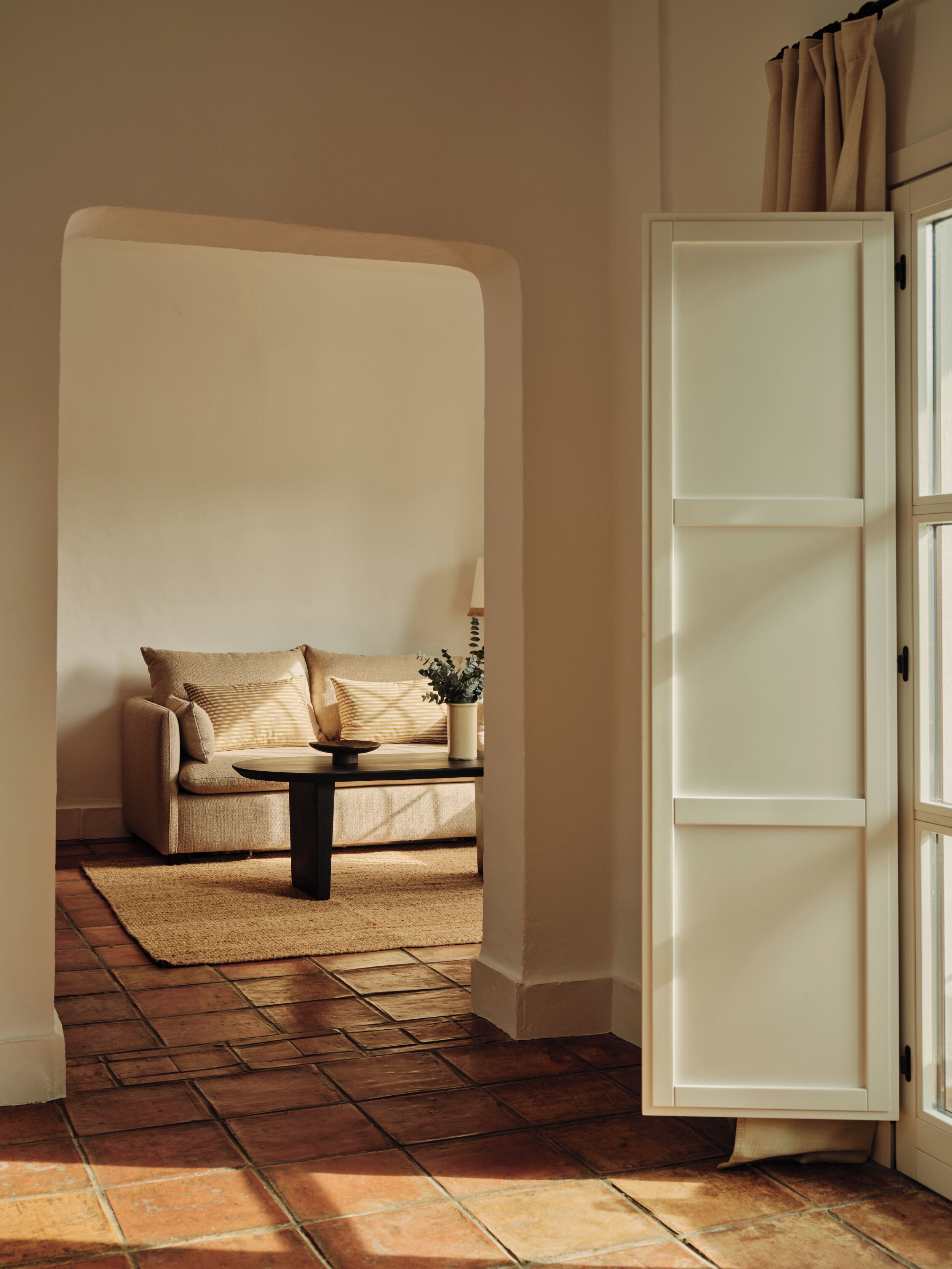 A room with a sofa, a small table, a potted plant, and a white cabinet.