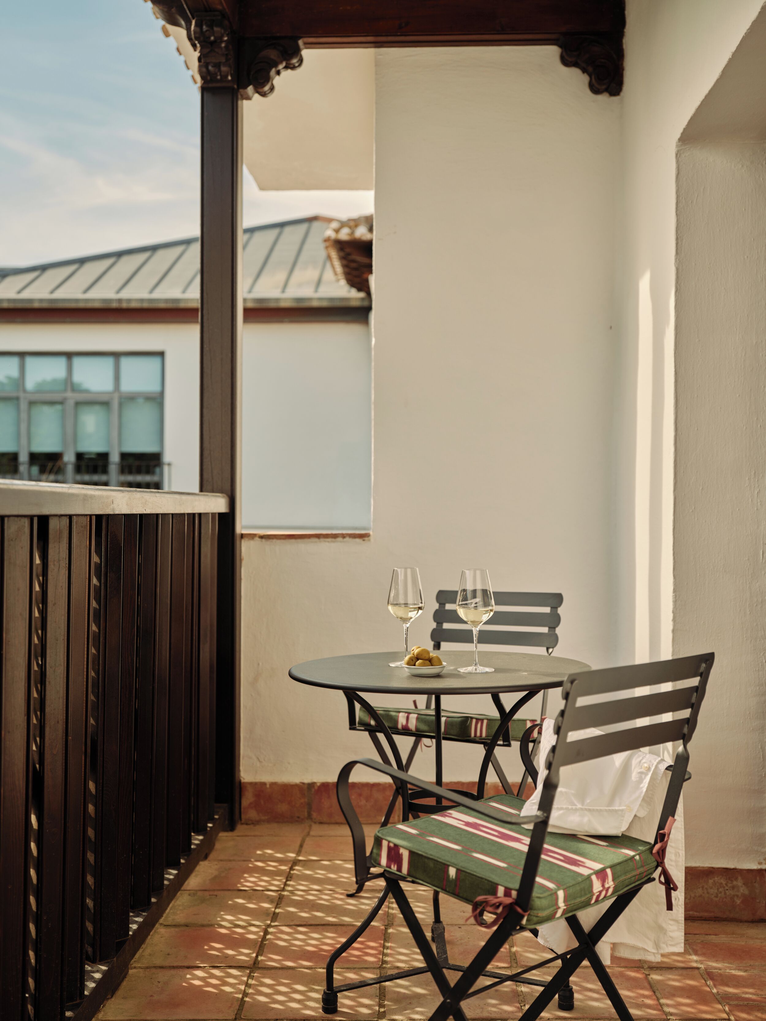 Een terras met een tafel, stoelen, twee wijnglazen en een schaal met snacks.