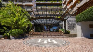 The entrance to Hotel Botánico with a circular mosaic design on the ground, a covered entrance, and a sign indicating the hotel is part of The Oriental Hotel Group.