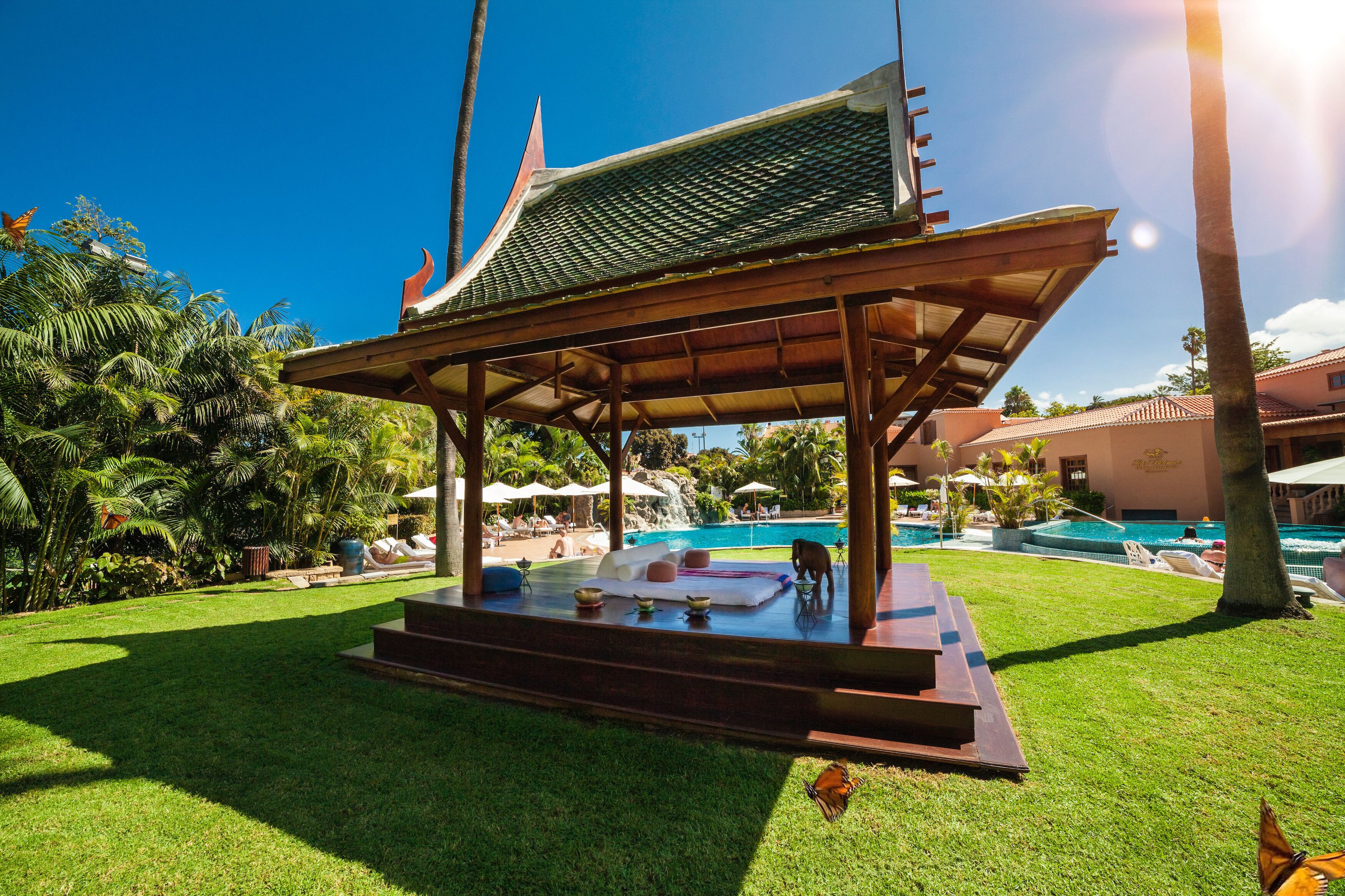 A traditional pavilion with a sloped roof, surrounded by a well-maintained lawn and palm trees.