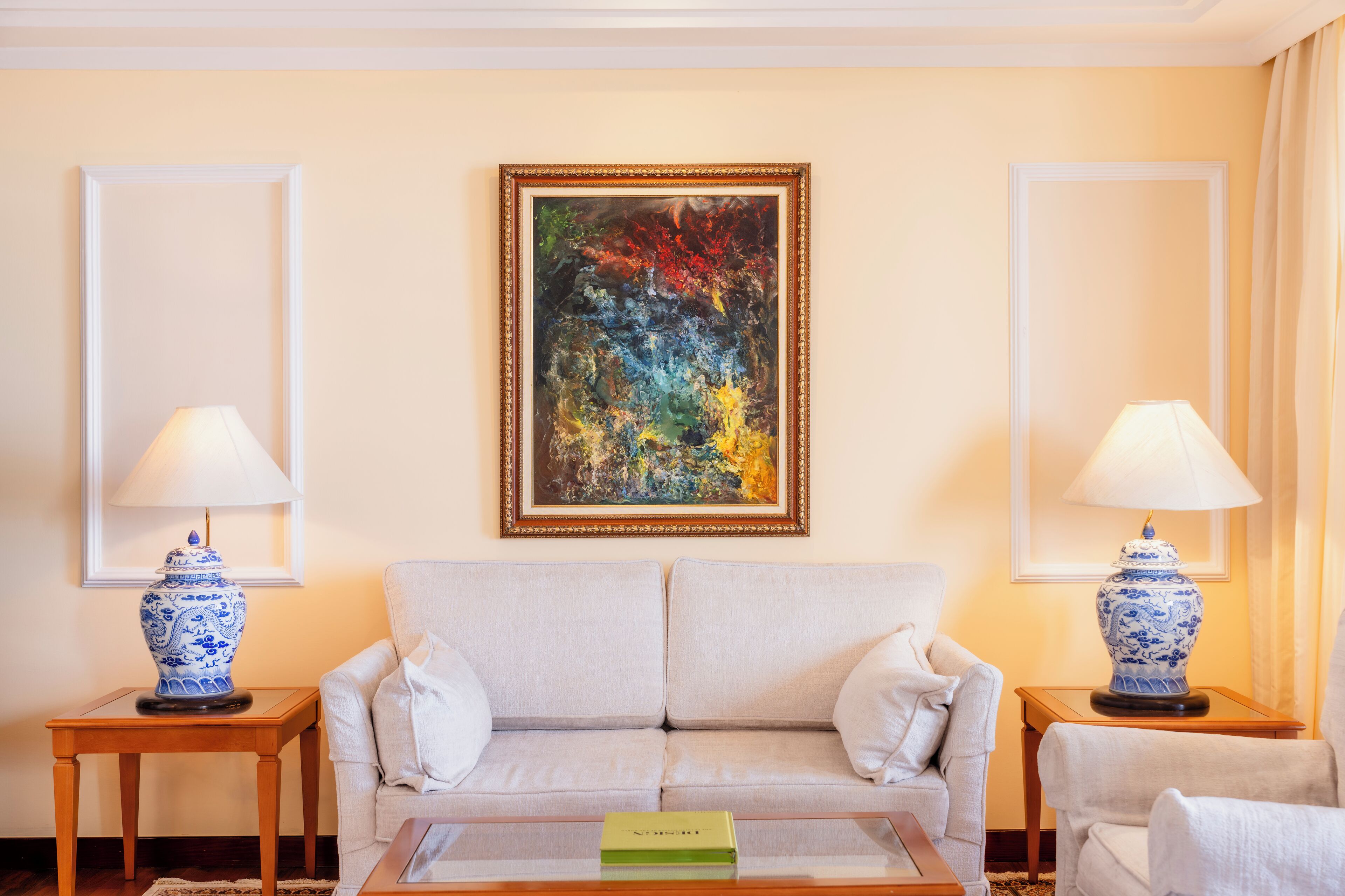 Un salón con un sofá color beige, dos lámparas azules y blancas a juego, y un cuadro abstracto de colores en la pared.