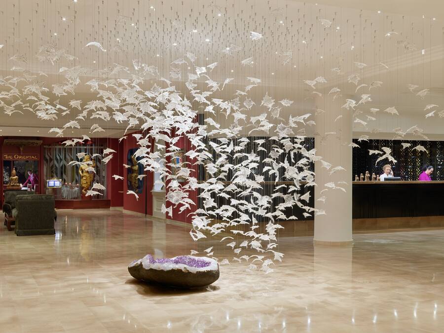 A lobby with a large, ornate statue, a reception desk, and a decorative ceiling installation.