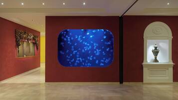 Un pasillo con un gran acuario azul decorativo, un adorno de pared y una urna clásica sobre un pedestal.