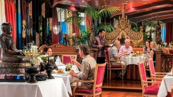 Un restaurante con suelo de madera, mesas con manteles blancos y un camarero atendiendo a los comensales.