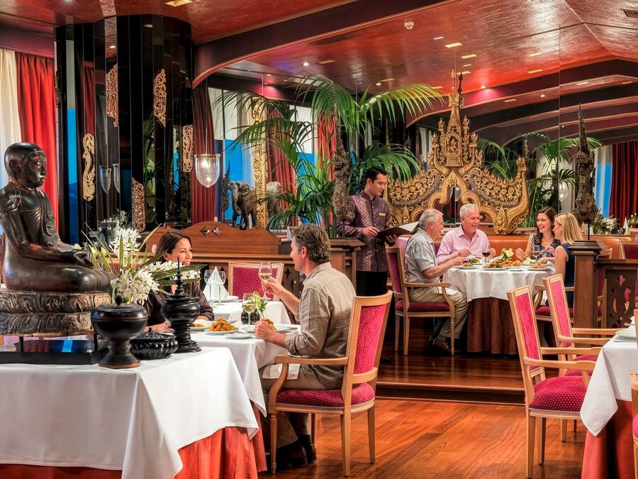 Un restaurante con suelo de madera, mesas con manteles blancos y un camarero atendiendo a los comensales.