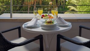 A table with a fruit platter, two glasses of orange juice, and a rose on a balcony overlooking a city and mountains.
