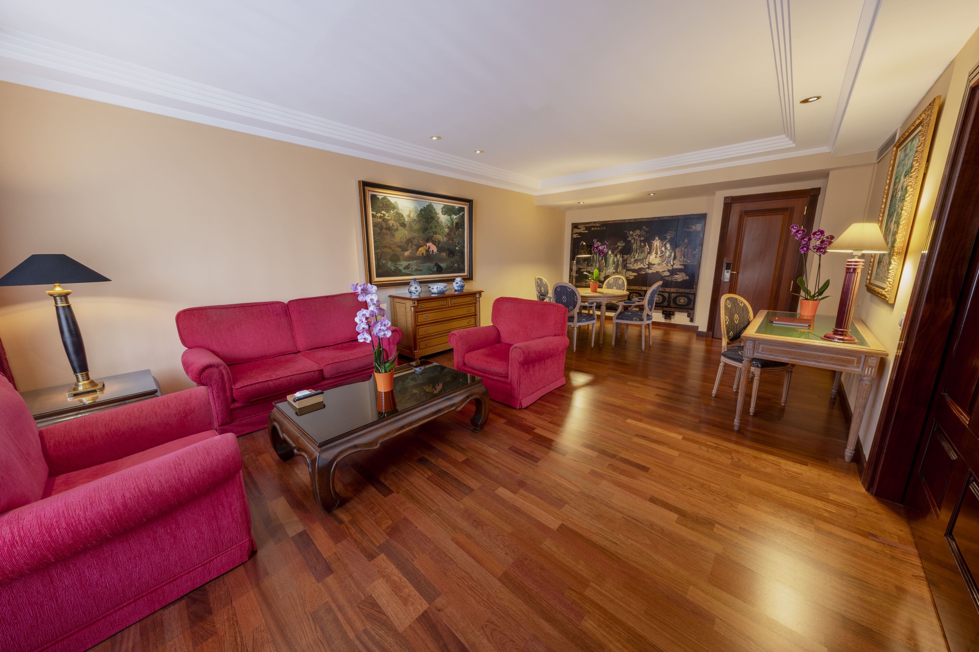 A spacious living room with a red sofa set, a coffee table, and a dining area with a table and chairs.