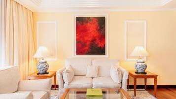 A living room with a beige sofa, two matching side tables, and a glass coffee table. A red abstract painting is centered on the wall above the sofa.