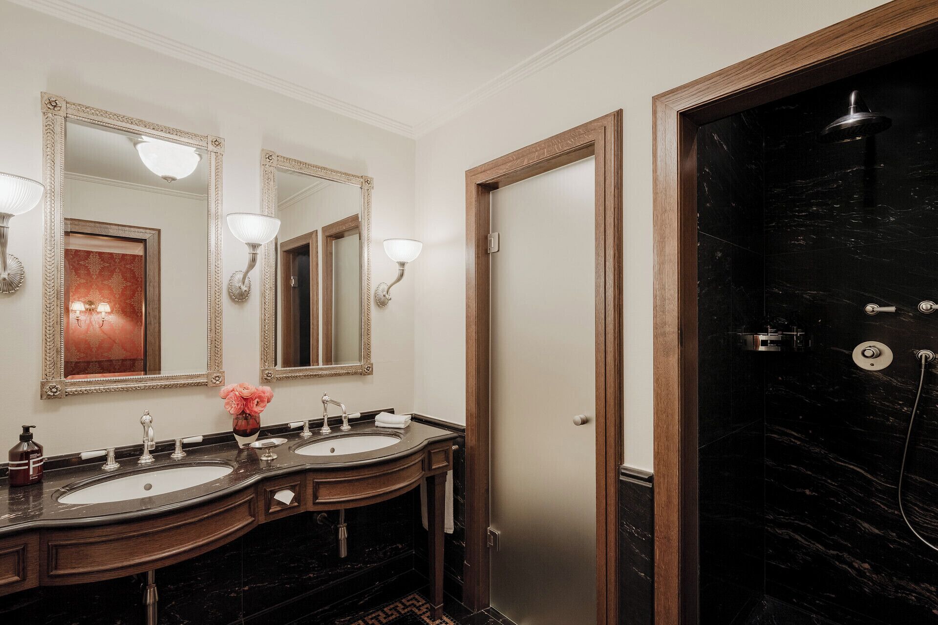 Ein Badezimmer mit zwei Waschbecken, einem Spiegel, Wandleuchten und einer Duschkabine.