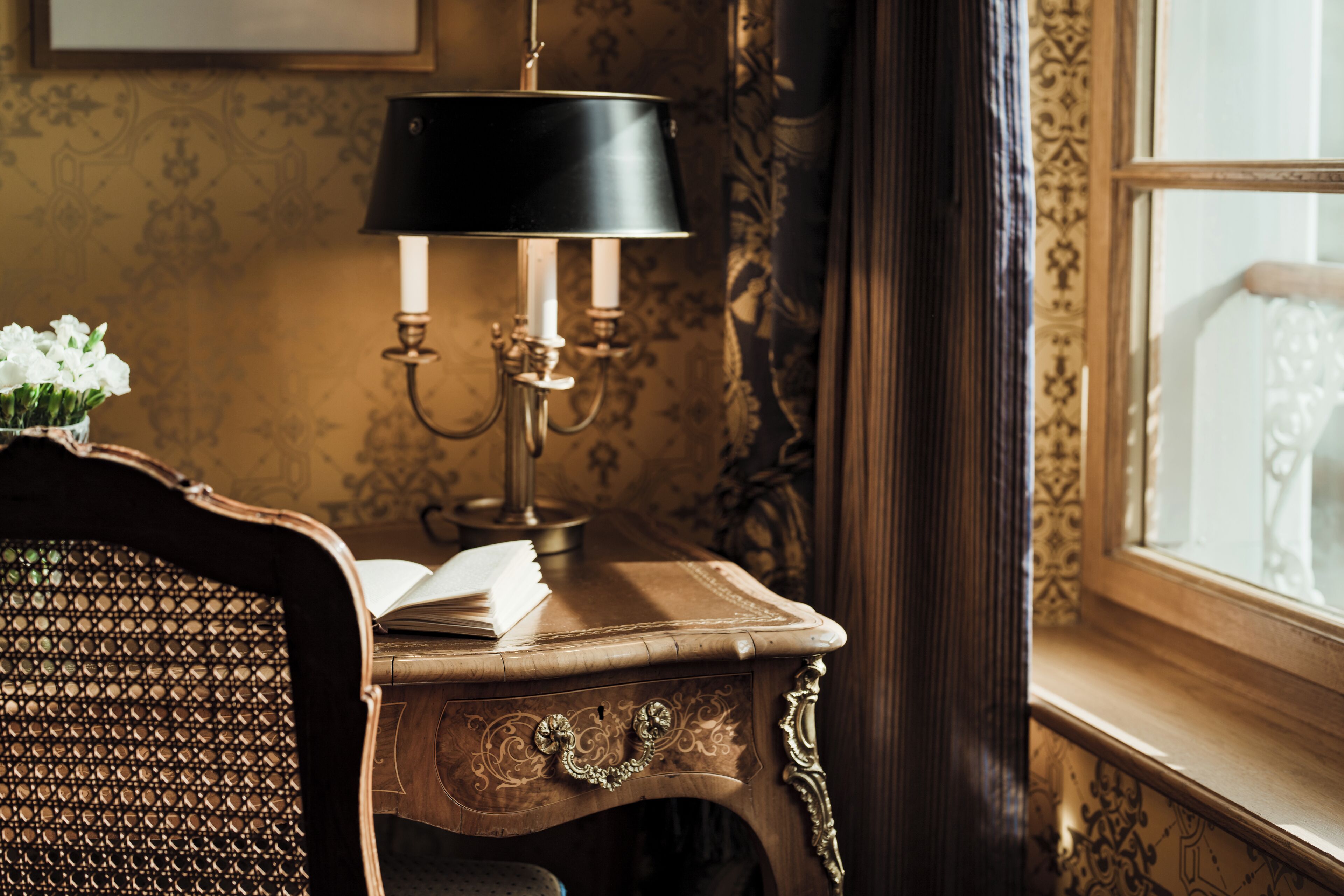 Et natbord i træ med en lampe, en åben bog og en vase med blomster.