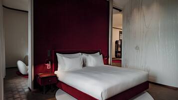 A modern bedroom with a large bed, a nightstand, a chair, and a red accent wall.