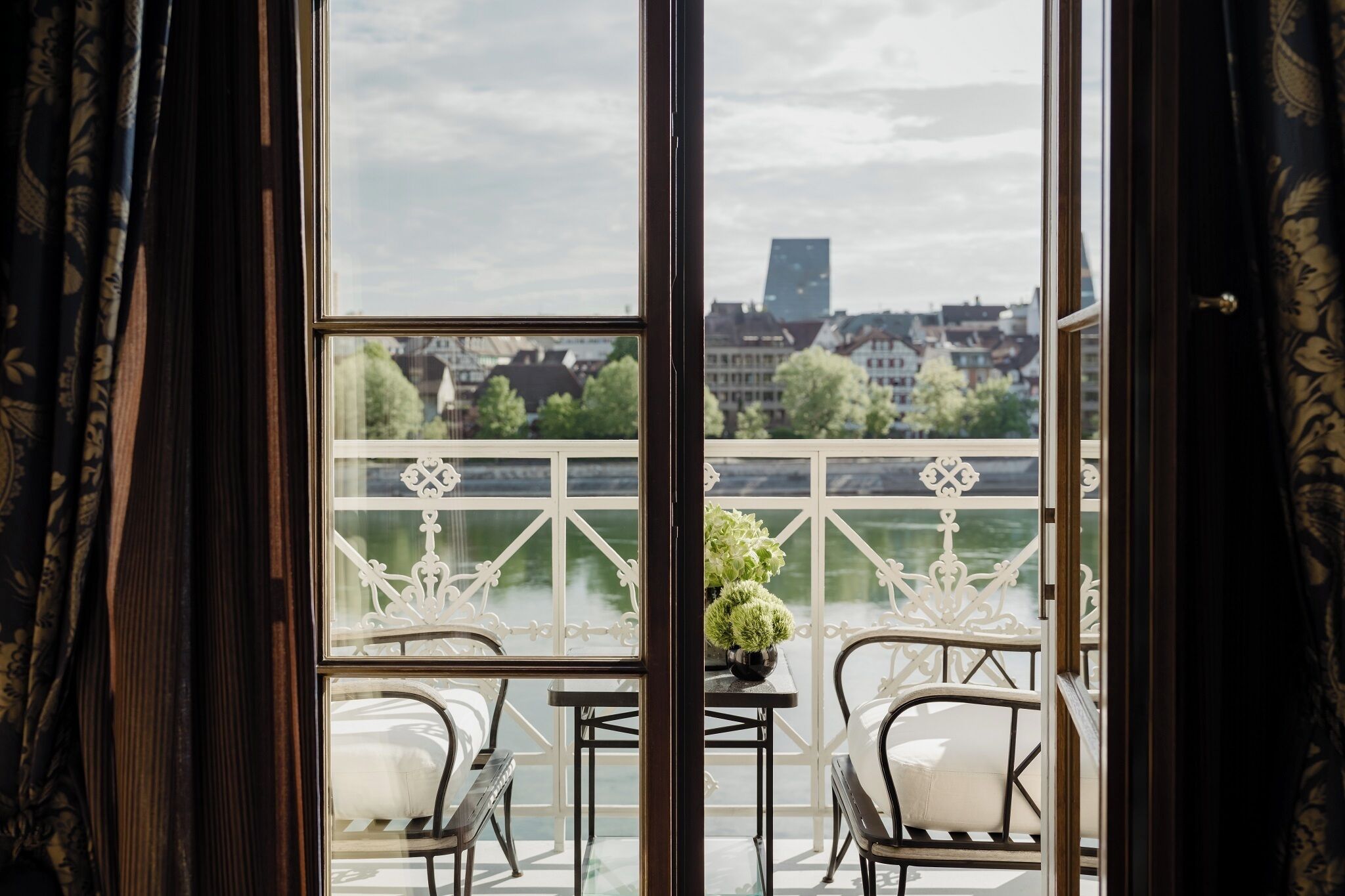 A balcony with a table and chairs, a view of a river, and buildings in the background.