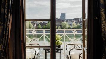 A balcony with a table and chairs, a view of a river, and buildings in the background.
