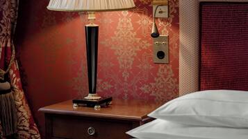 Un lit bien fait, avec du linge de lit blanc, une lampe de chevet, une table de chevet en bois, une horloge murale et un mur décoré d’un motif rouge.