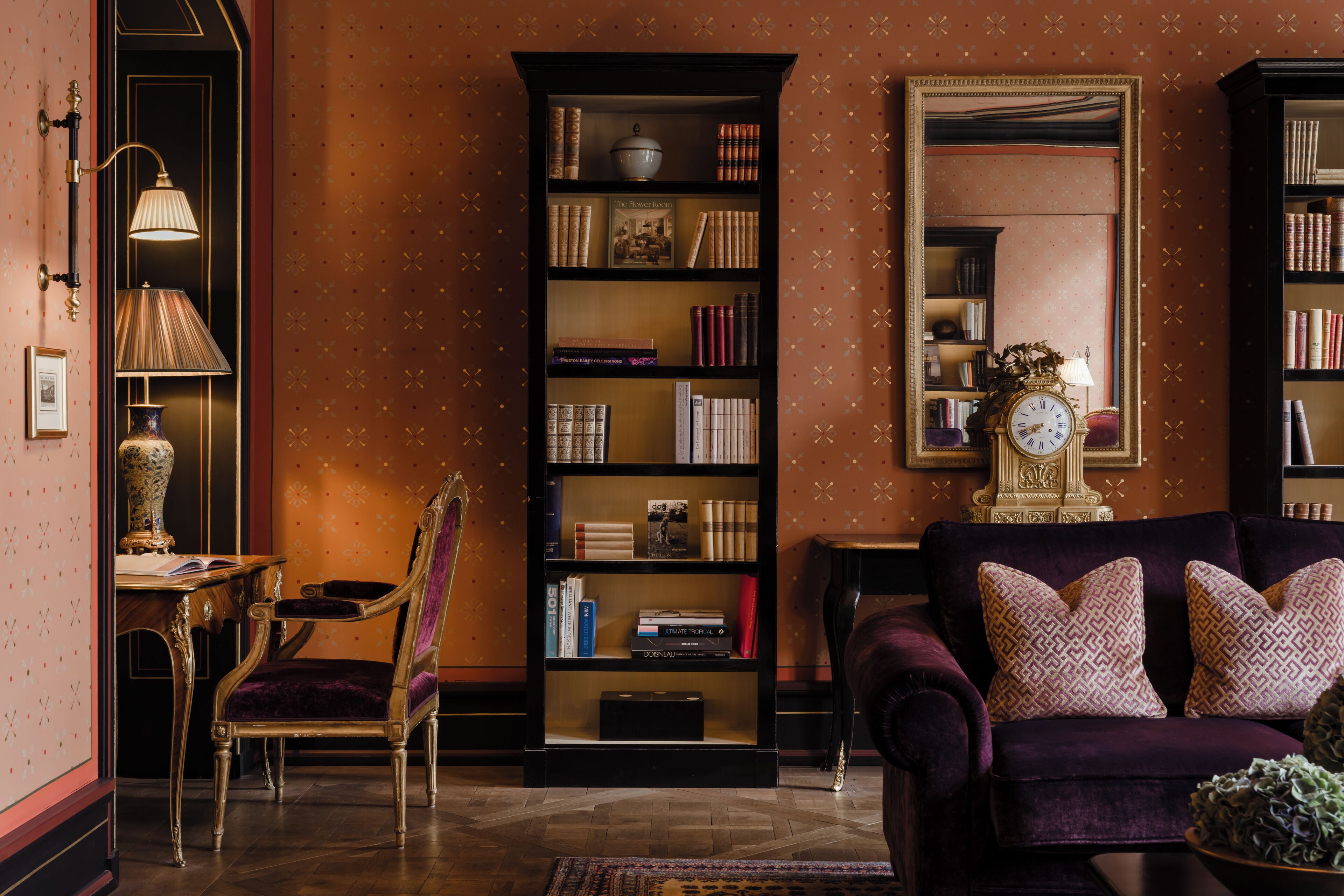 Una habitación con una amplia estantería, una silla, un sofá y un espejo.