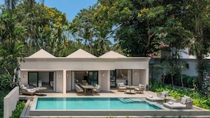 Una casa moderna con piscina, mobiliario exterior y exuberante vegetación.