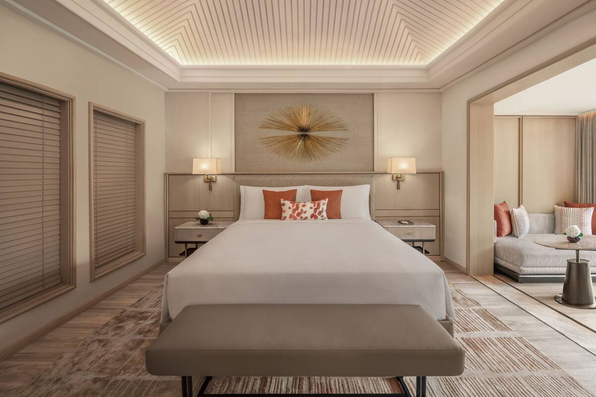 Une chambre d’hôtel avec un grand lit, un banc, une lampe fixée au mur et un élément décoratif mural.