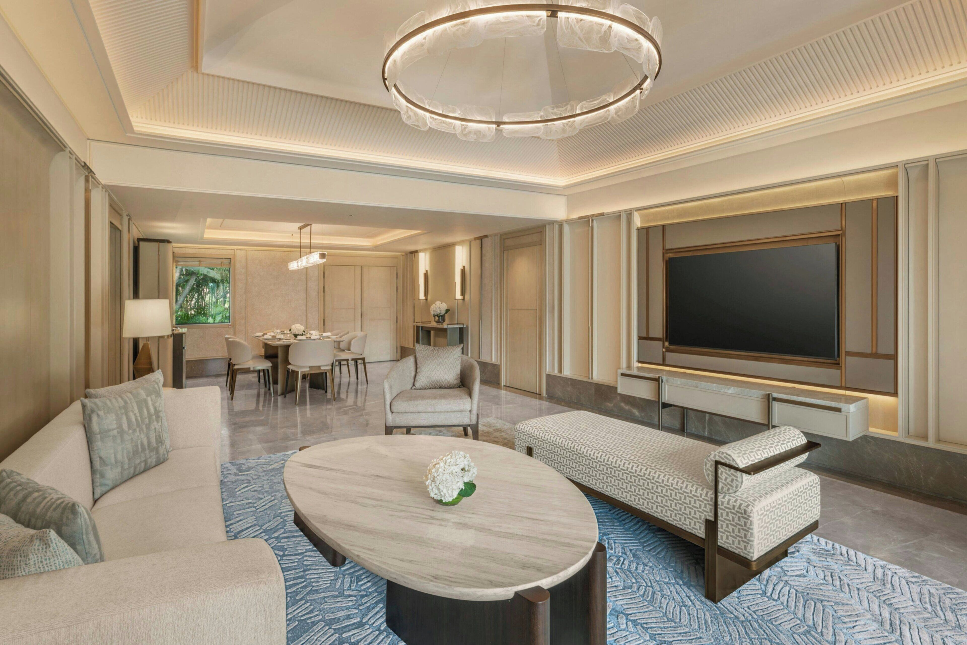 A modern hotel room with a large flat-screen TV, a dining area, a sofa, and a coffee table.