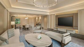 A modern hotel room with a large flat-screen TV, a dining area, a sofa, and a coffee table.