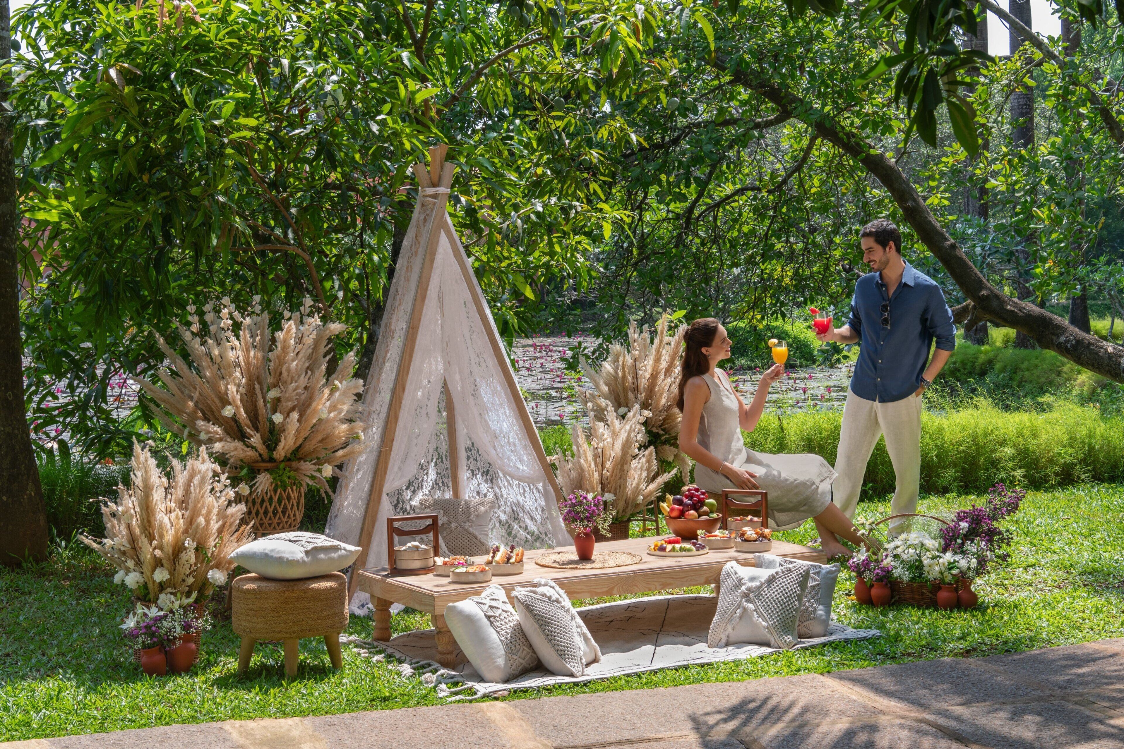 Montagem para piquenique com uma tenda, mesa de jantar e cadeiras em um jardim exuberante.