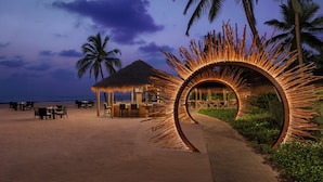 Un restaurante junto a la playa con una cabaña de techo de paja y una estructura circular iluminada.