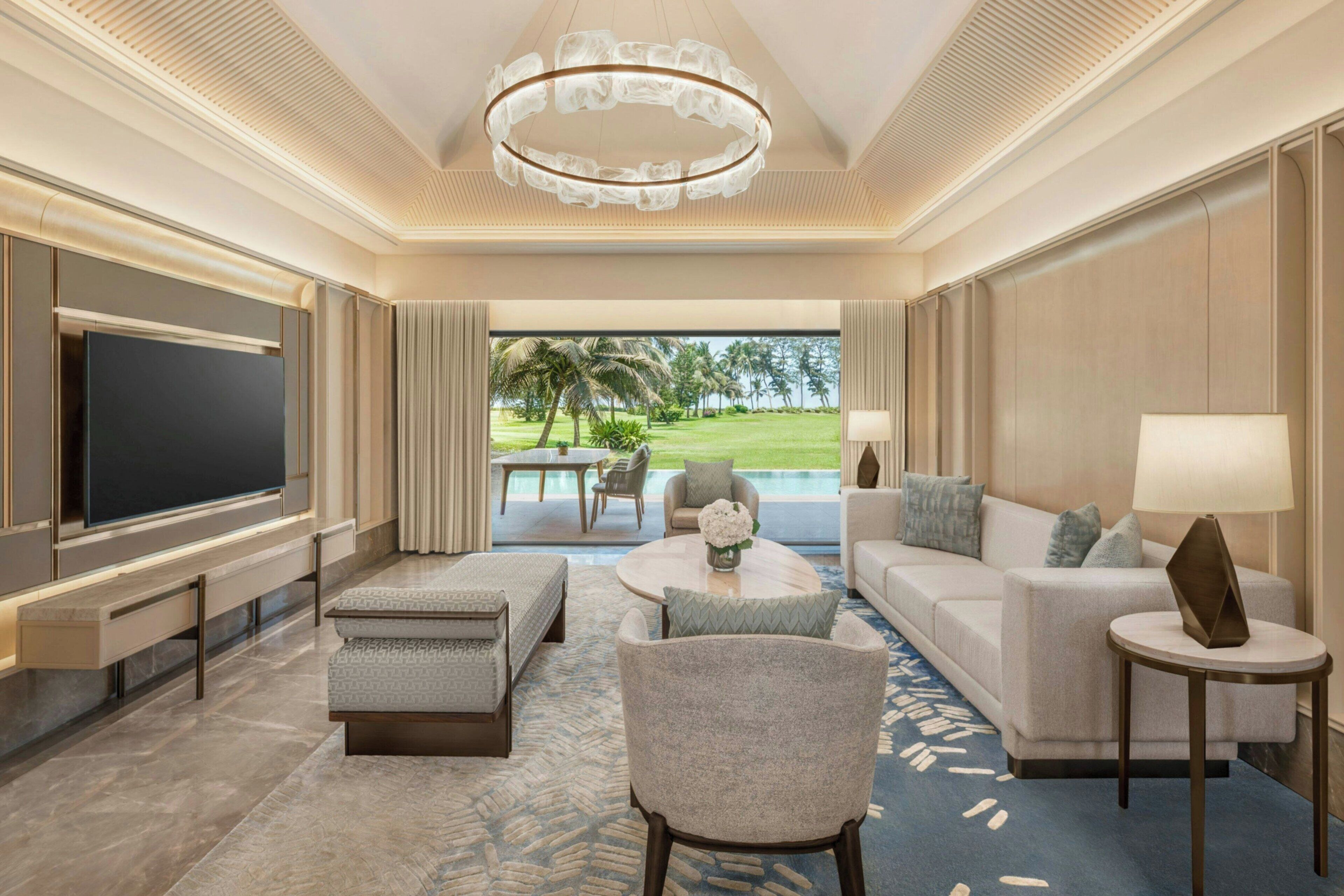 A spacious living room with a large flat-screen TV, comfortable seating, a coffee table, and a view of a golf course through large windows.