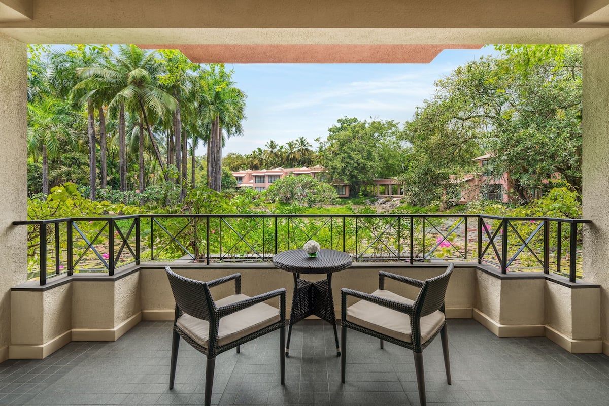A covered outdoor seating area with a table and chairs, surrounded by lush greenery and a view of buildings in the distance.