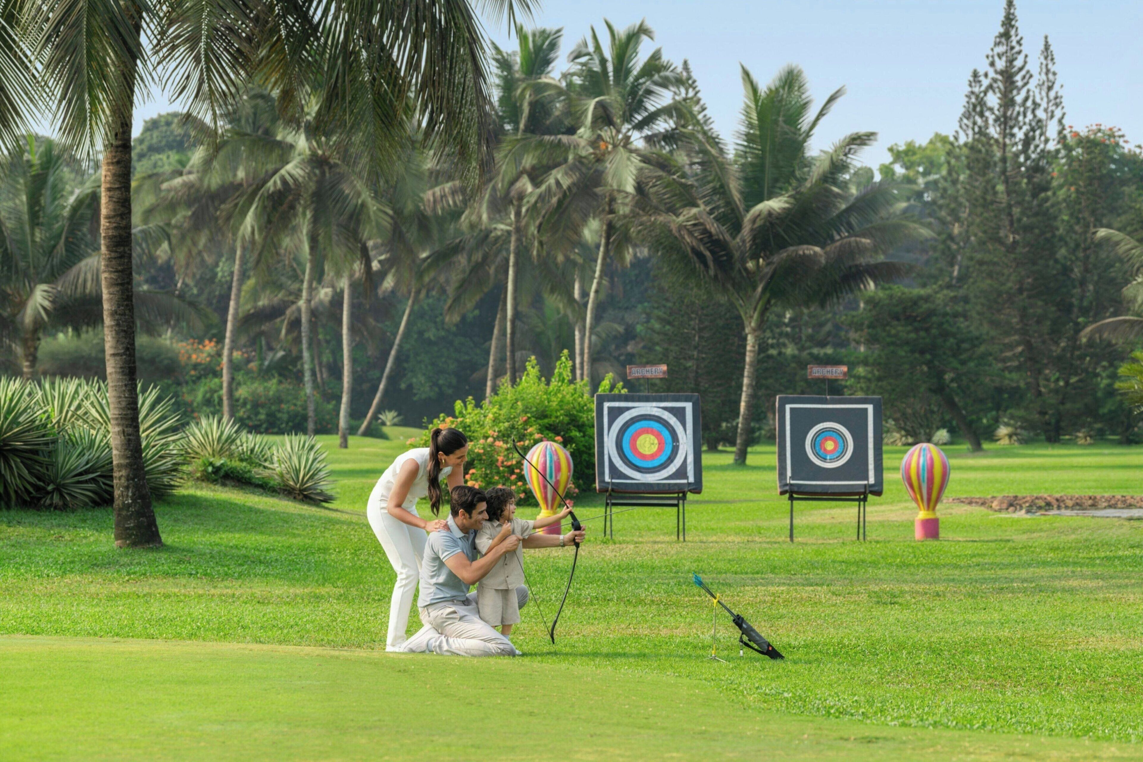 A golf course with targets, palm trees, and a person aiming a bow.