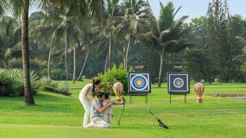 A golf course with targets, palm trees, and a person aiming a bow.
