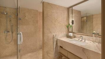Un baño moderno con ducha envuelta en vidrio, pared de azulejos de mármol, un espejo grande y un mueble de tocador de madera con lavamanos.
