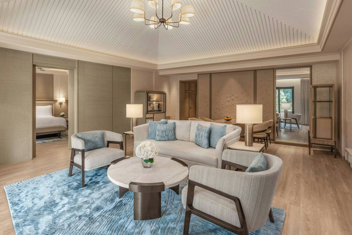 Une chambre d’hôtel moderne comprenant un canapé, deux fauteuils, une table basse et un coin repas avec une table et des chaises.