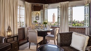 A room with a round table, two chairs, a sofa, and a view of a tower. - La Mamounia (Marrakech)