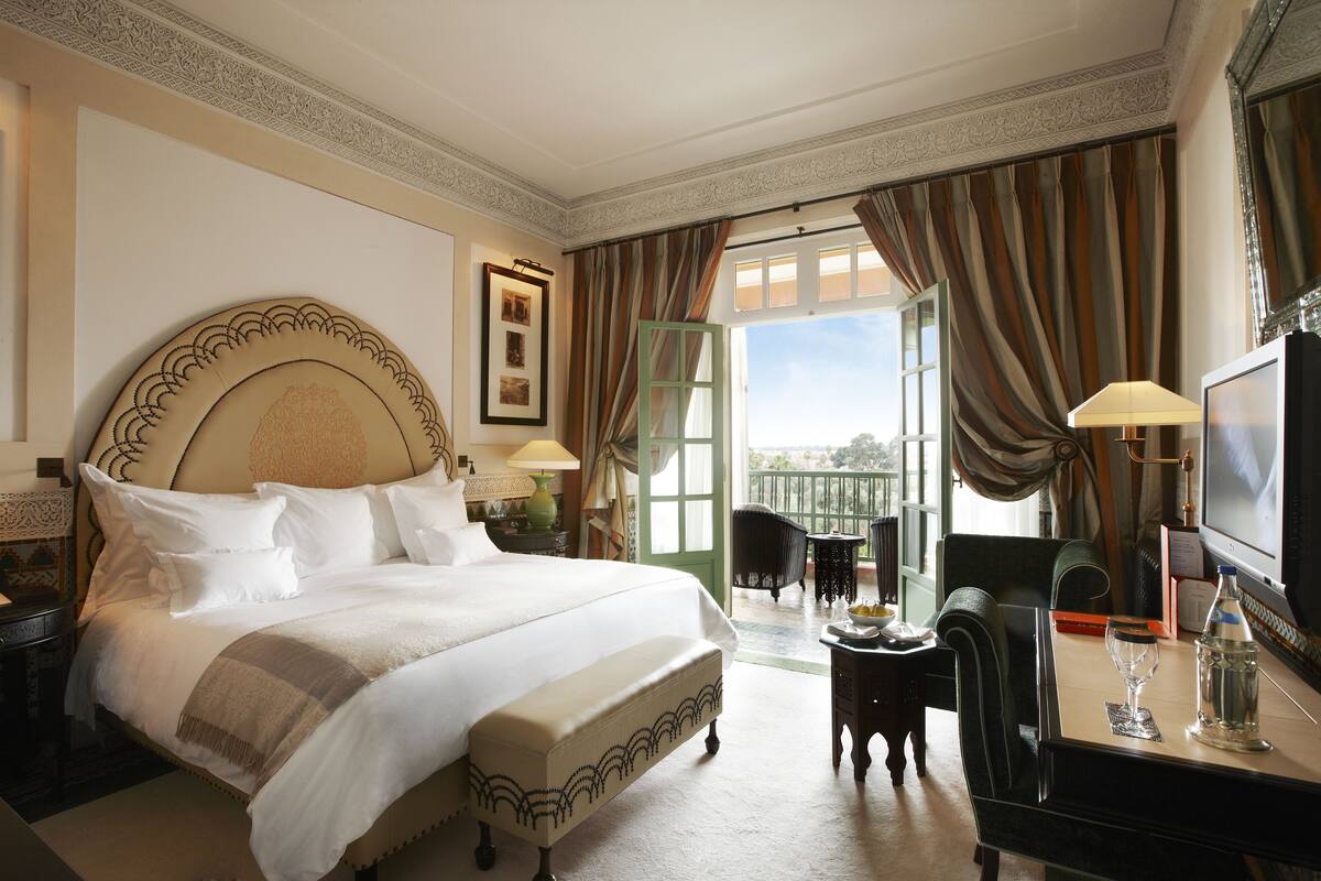 Una camera d'albergo con un letto grande, una scrivania con una sedia, una televisione e un balcone con tende.
