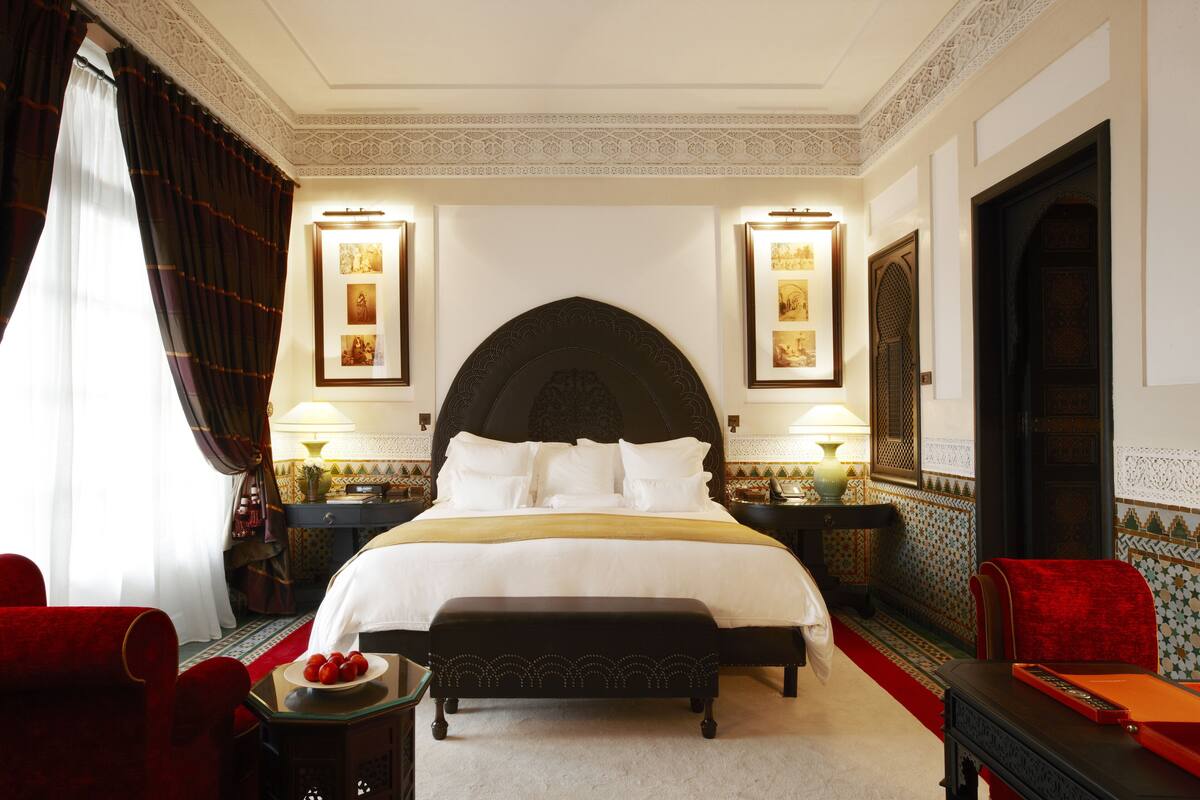 Camera d'albergo con un letto grande, due comodini, una poltrona rossa, una panca e un divano rosso.