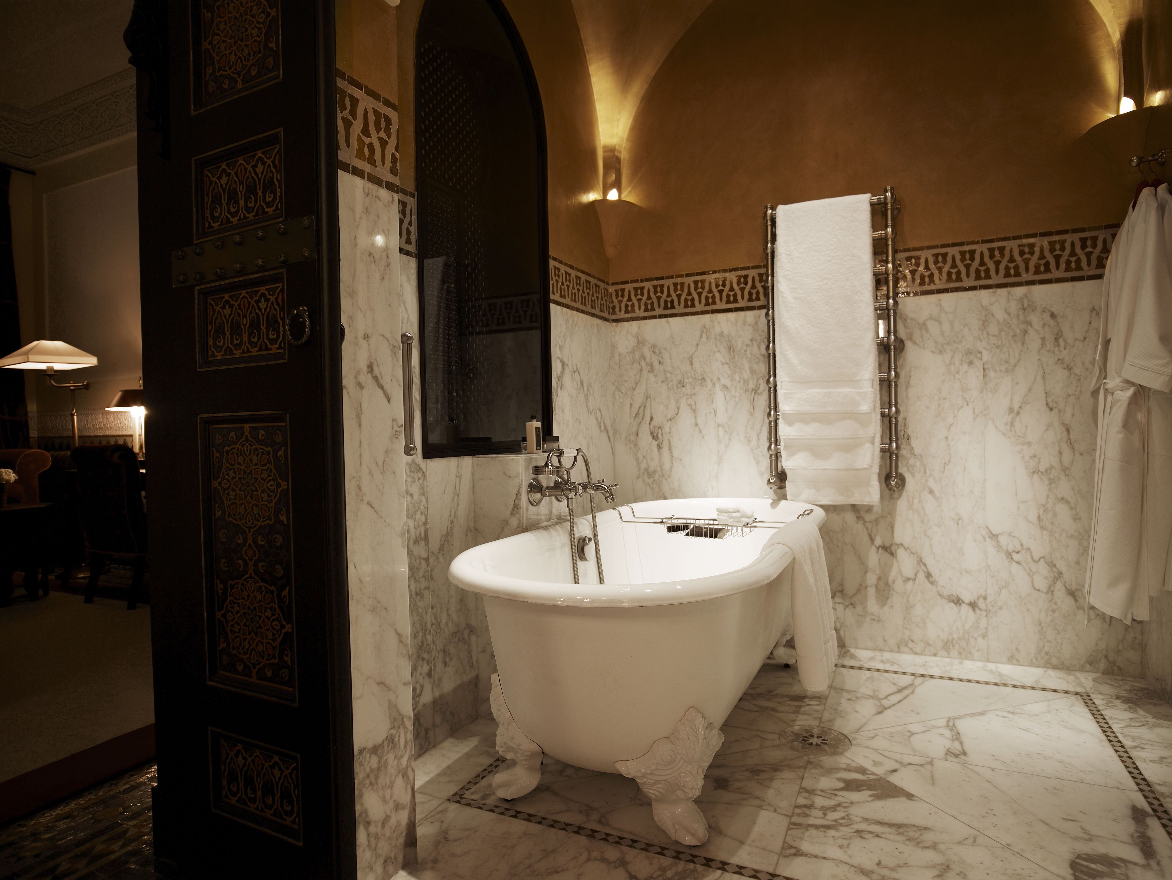 A luxurious bathroom with a freestanding bathtub, marble walls, and a large mirror.