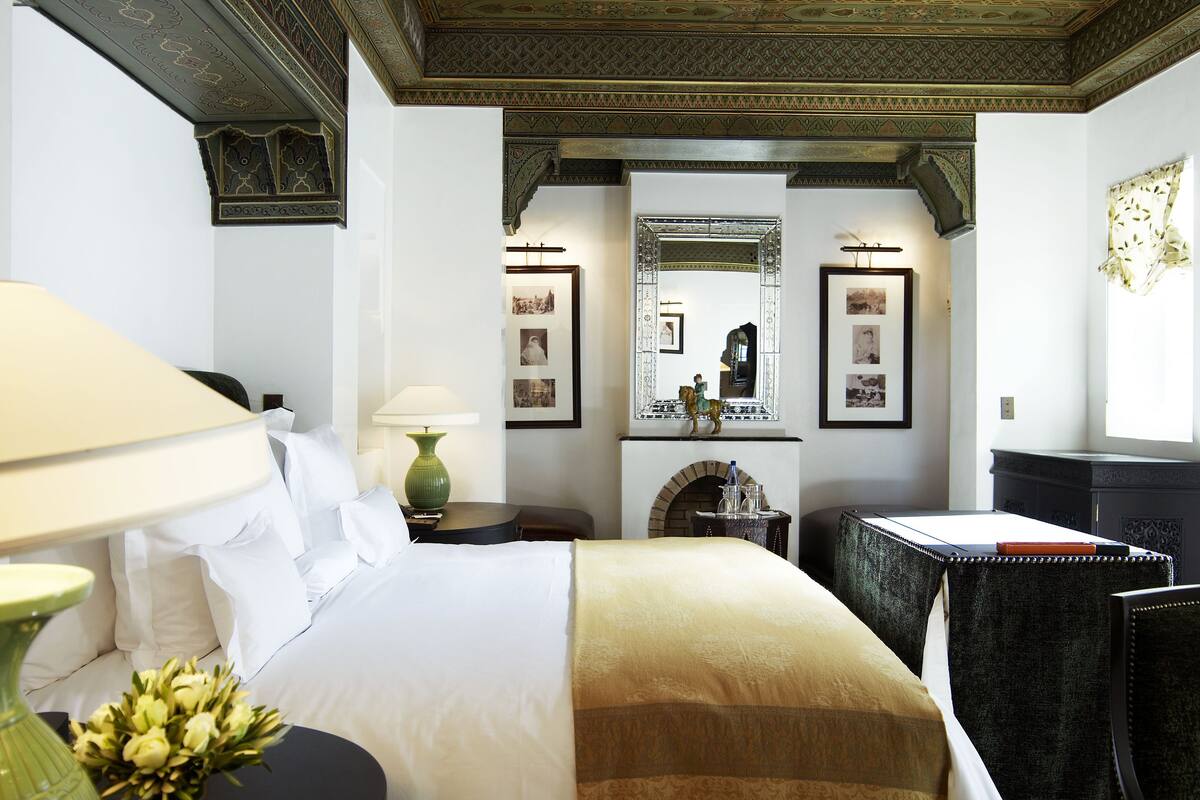 Una camera d'albergo con un letto grande, una scrivania, una sedia, una lampada e un soffitto decorato.