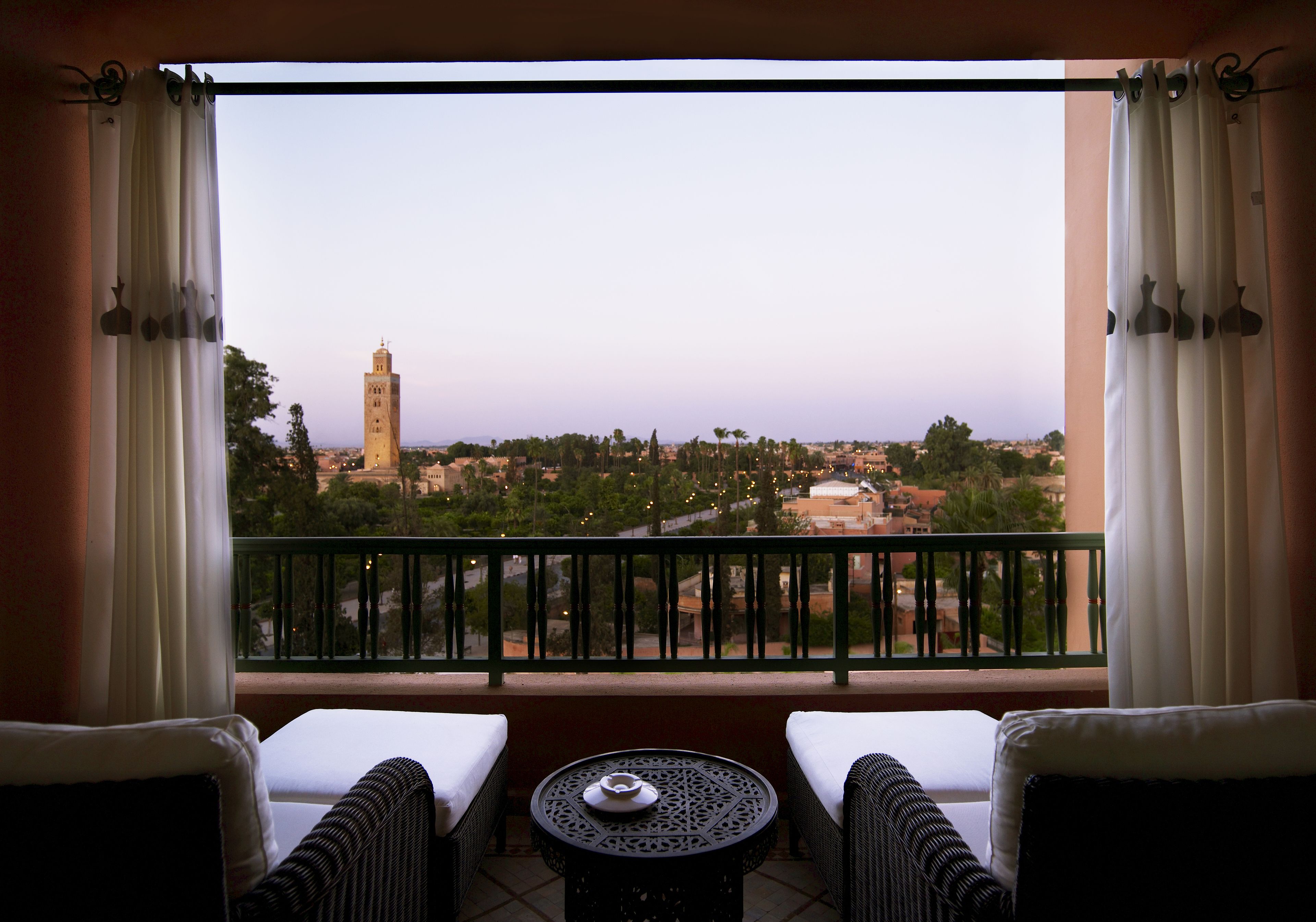 A balcony with two wicker sofas and a small round table, overlooking a cityscape with a prominent tower.