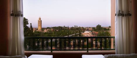 A balcony with two wicker sofas and a small round table, overlooking a cityscape with a prominent tower.