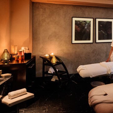 A spa room with a massage table, towels, candles, and framed artwork on the wall.