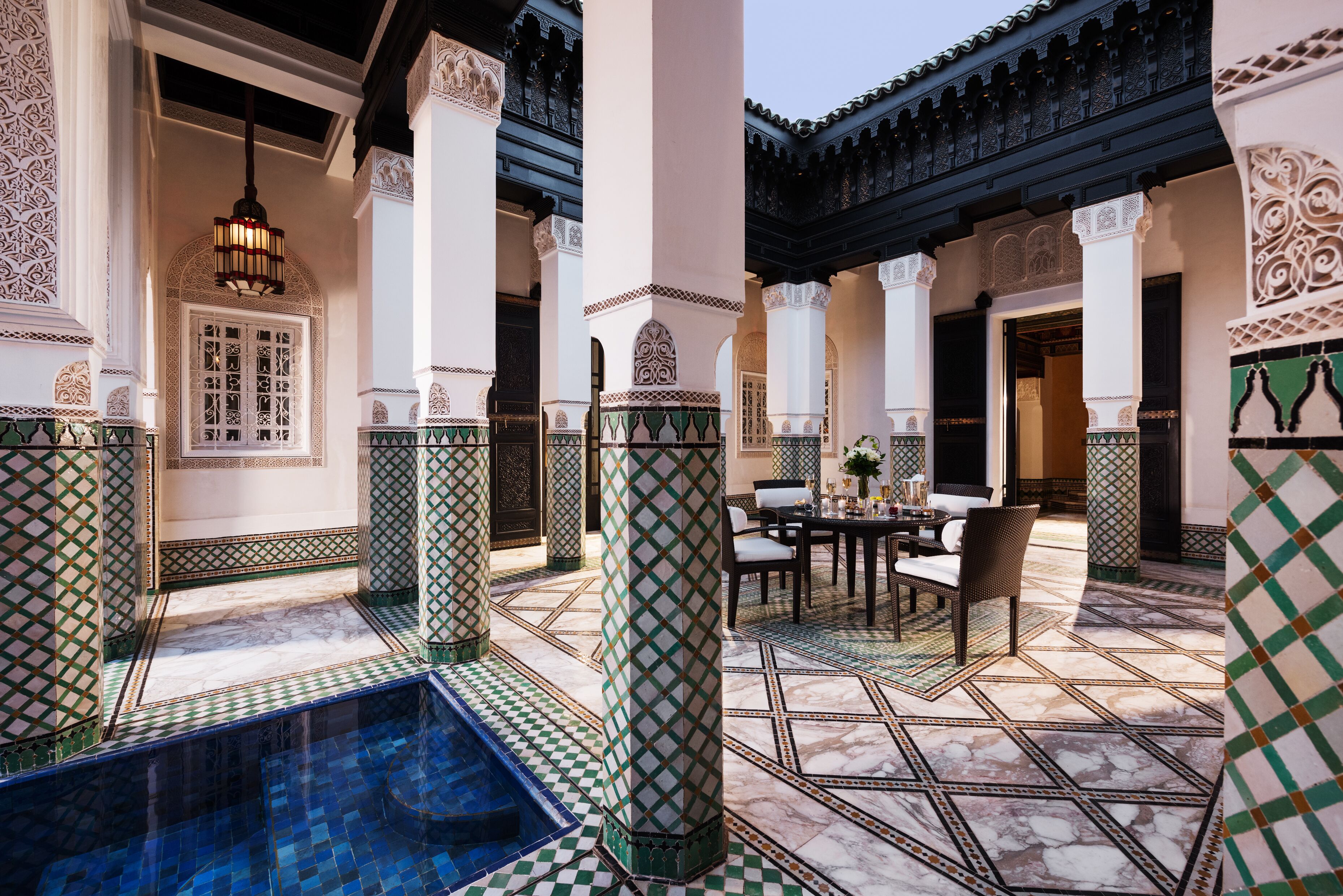 Un cortile con piscina, pavimento piastrellato e zona pranzo con sedie e tavolo.