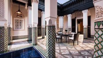 Un cortile con piscina, pavimento piastrellato e zona pranzo con sedie e tavolo.