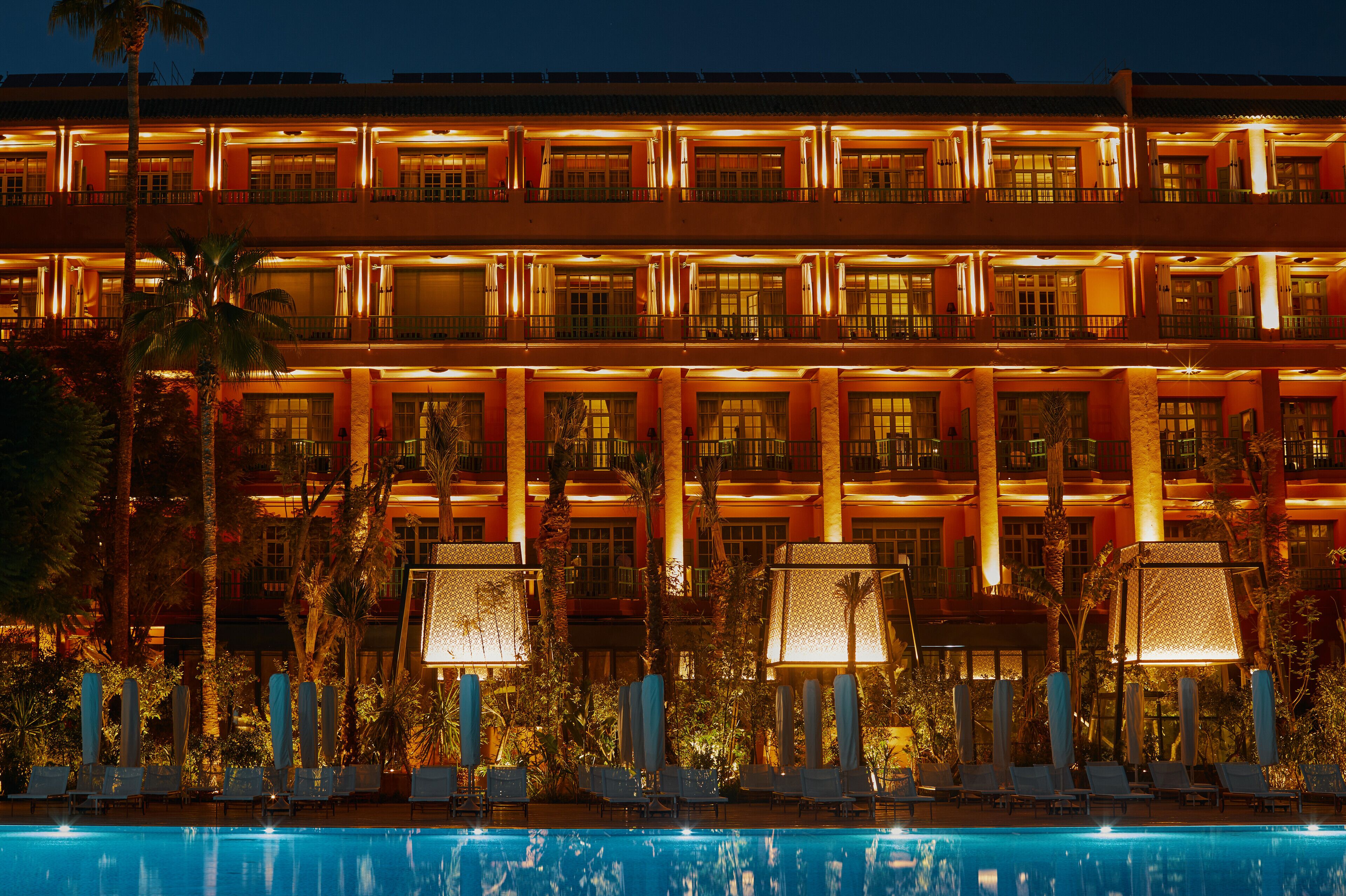 Un hotel de varios pisos con zona de piscina, sillas de descanso y sombrillas.