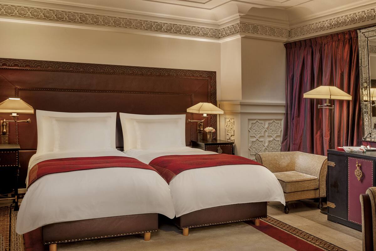 Un letto matrimoniale con una coperta rossa, un comodino con una lampada, una sedia, un comò e un grande specchio.