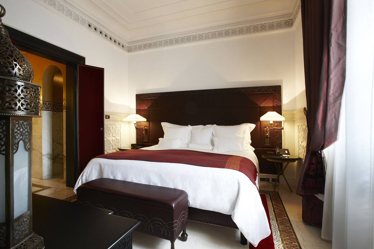 Camera d'albergo elegante con un letto grande, due lampade da comodino, una panca e un elemento decorativo a parete.