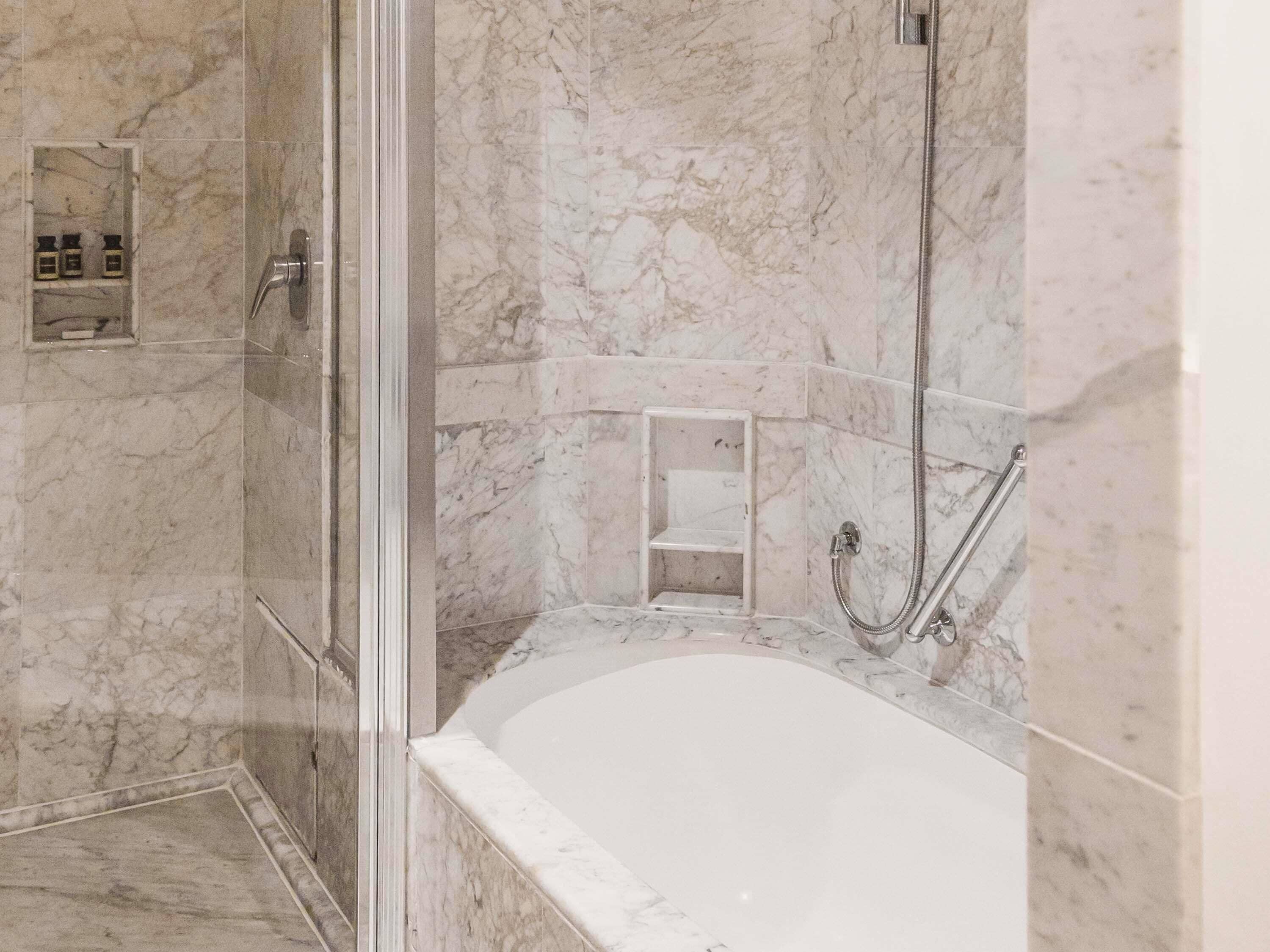 Une salle de bain avec un sol en marbre, une baignoire, un espace douche et une cabine de douche en verre.