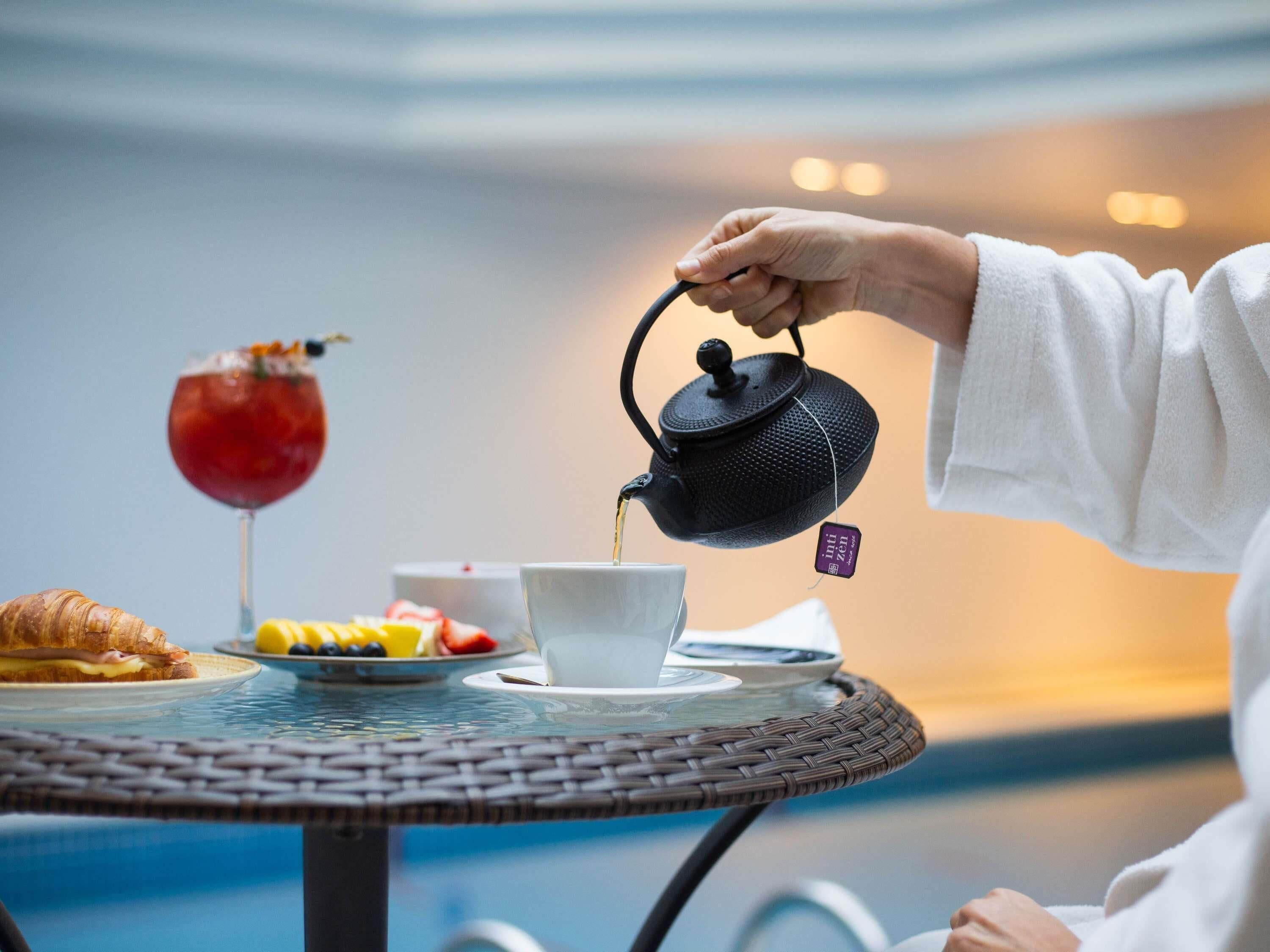 A person pouring tea into a cup on a round table with a wicker edge.