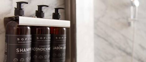 Tres botellas de champú, acondicionador y gel de ducha Sofite sobre una pared de mármol.