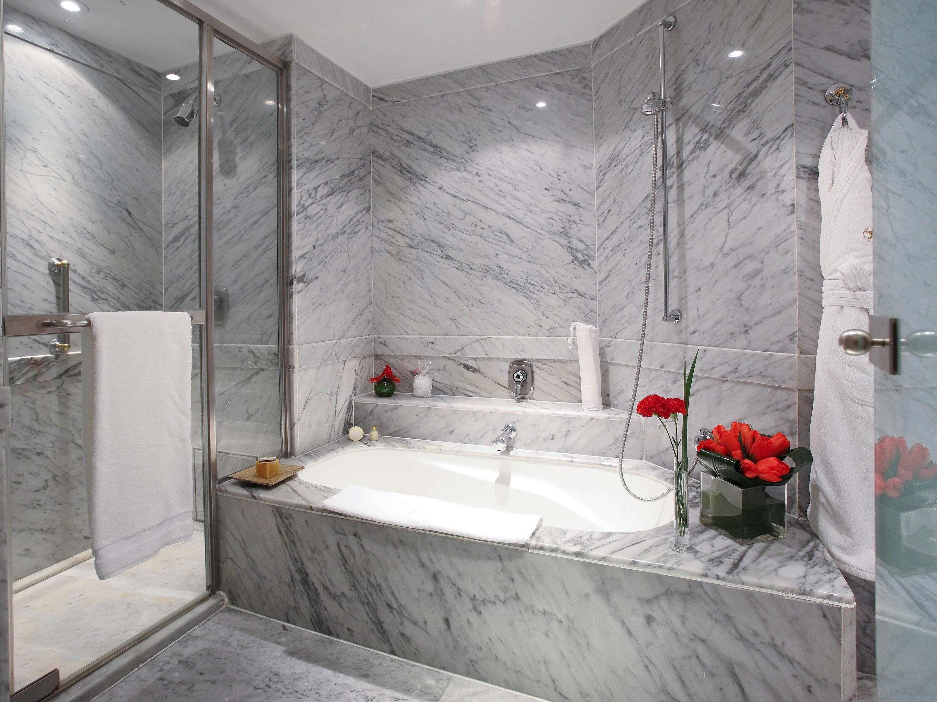 A modern bathroom with a glass-enclosed shower, a freestanding bathtub, and marble walls.