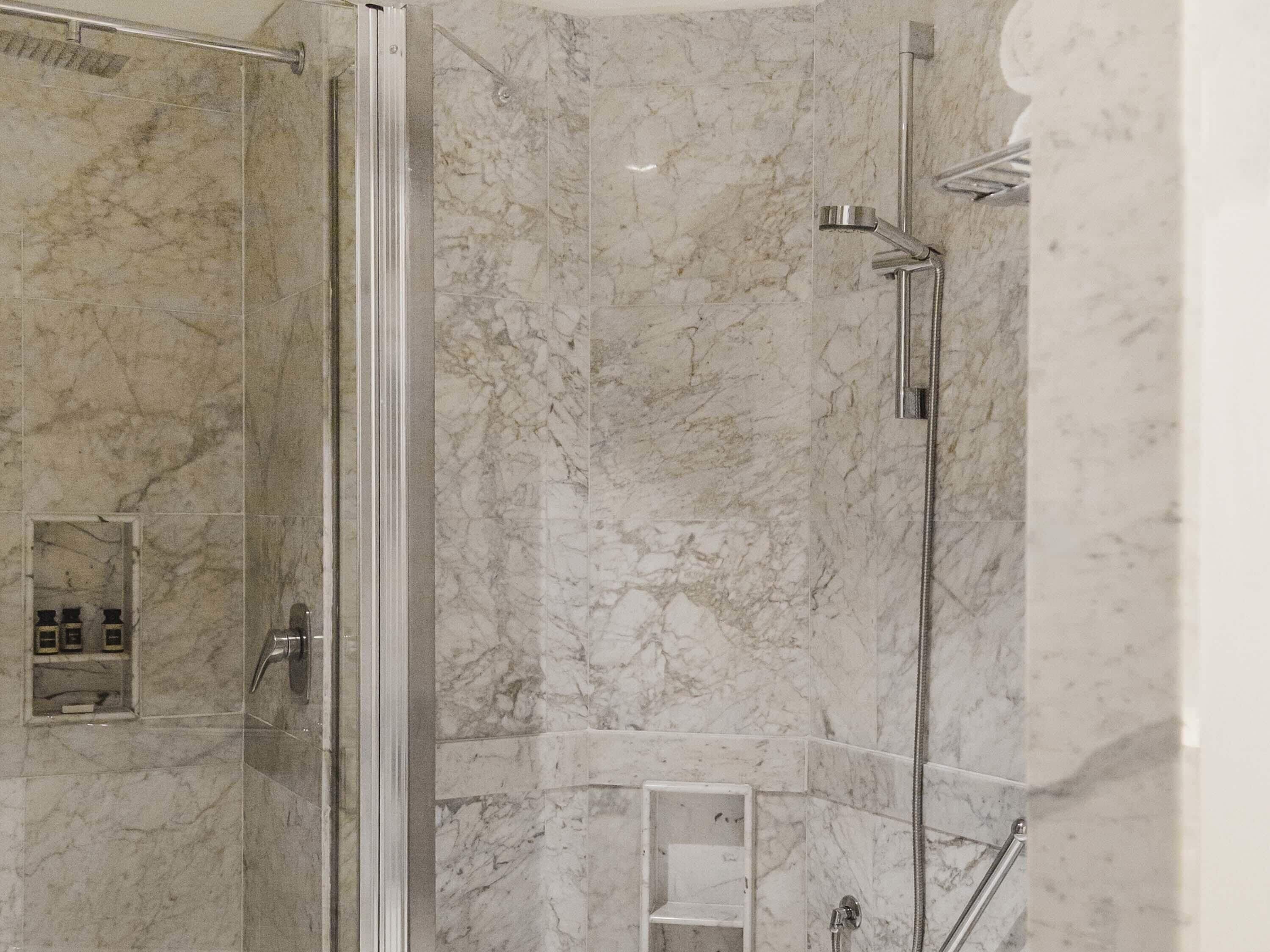 A modern bathroom with marble walls and a glass shower enclosure.