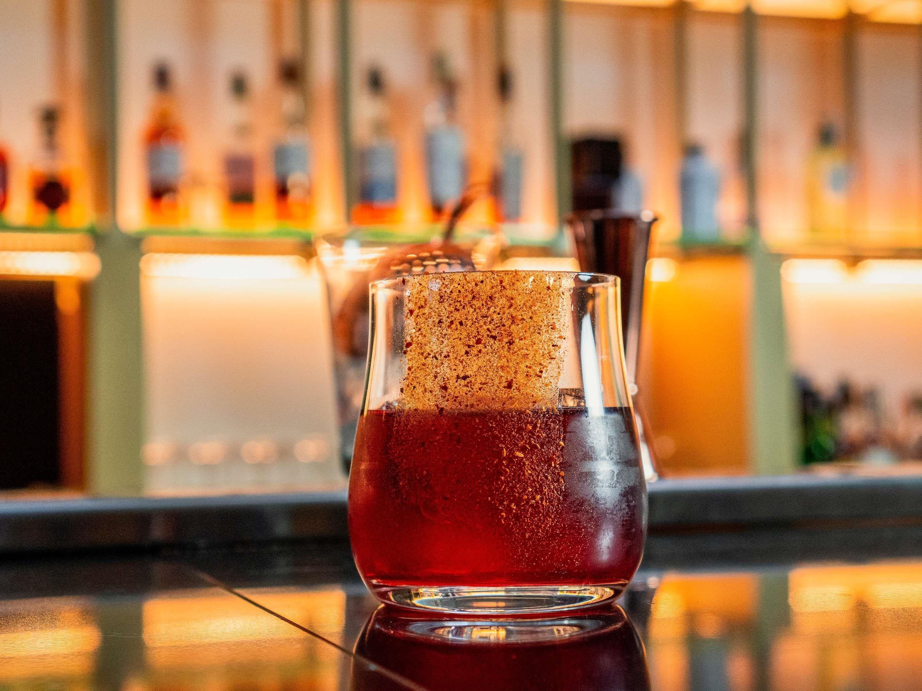 A bar setting with a glass containing a dark beverage, a frothy top, and a straw.